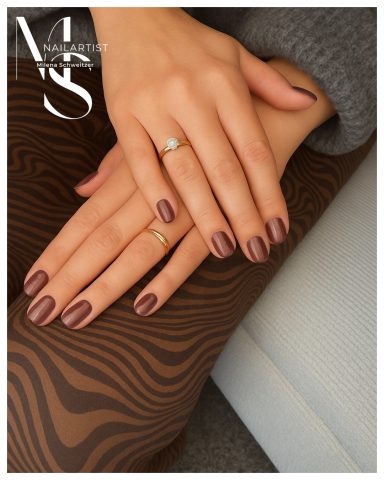 Hochwertige Maniküre mit braunem Nagellack und zarten Ringen auf elegantem Hintergrund.