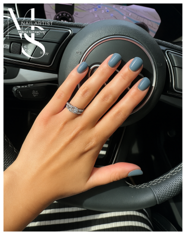 Hand mit blauen Nägeln und Ring, auf dem Lenkrad eines Autos.